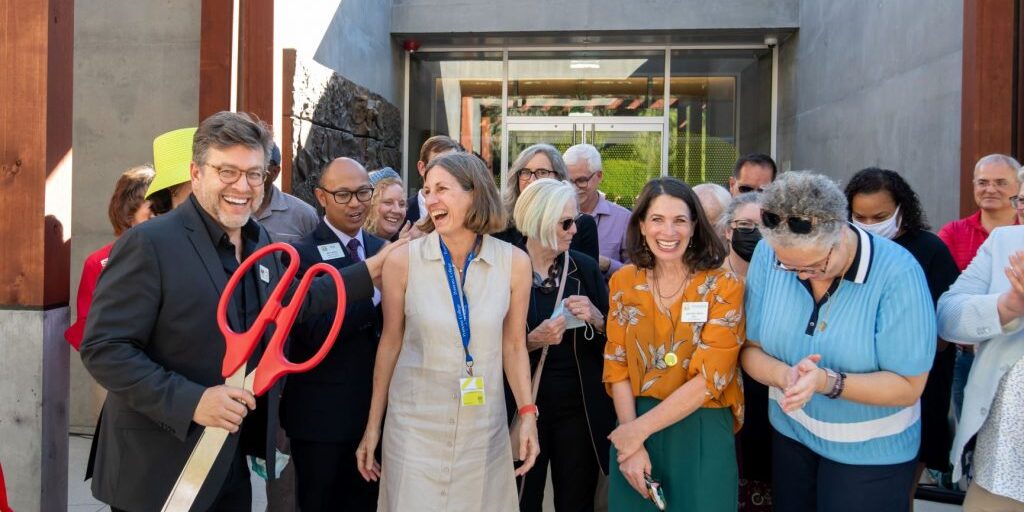 A group of Claremont Chamber Members at a ribbon cutting ceremony smiling and laughing